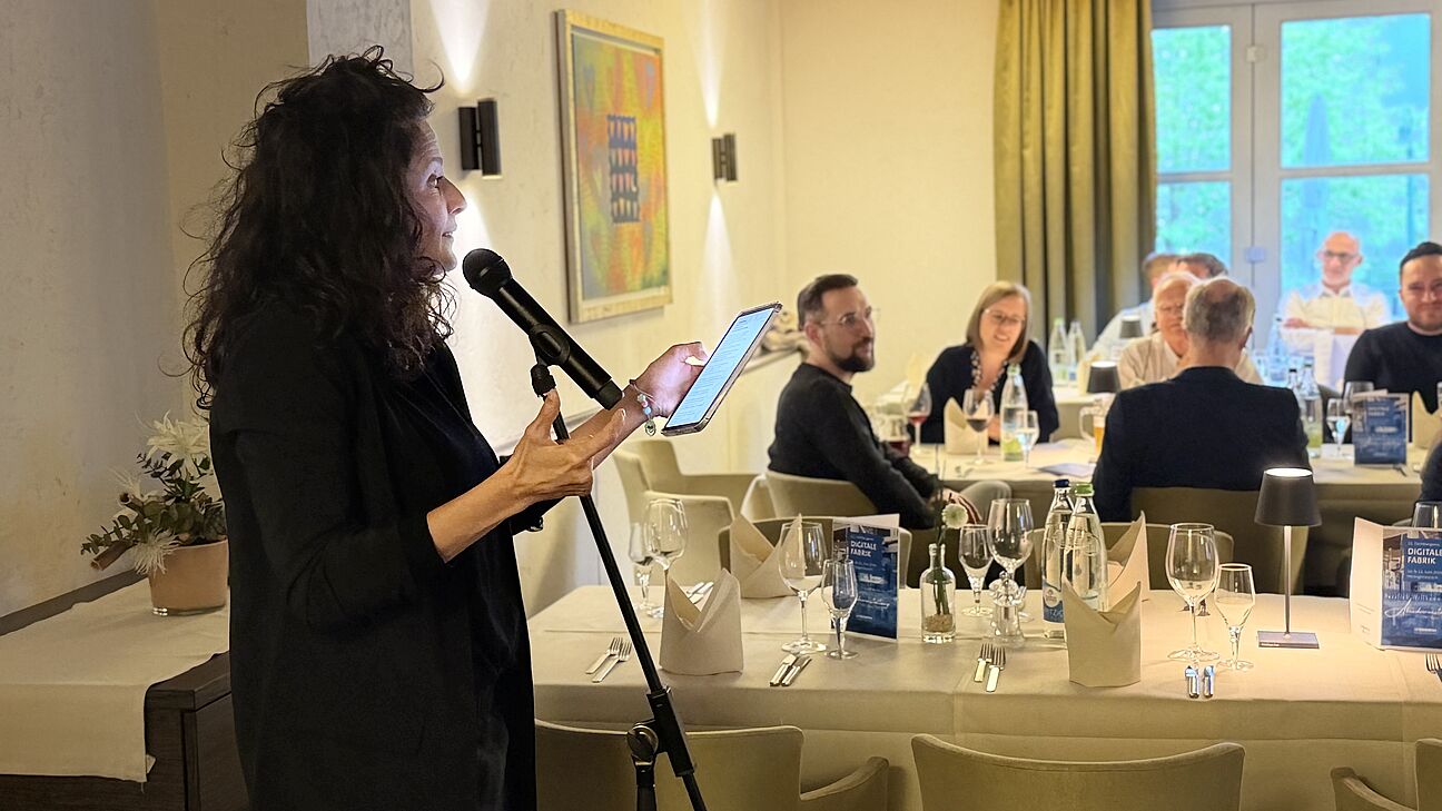 Digitale Fabrik 2026 - eine Dame singt den Teilnehmern in der Abendveranstaltung was vor und singt Richtung Tische